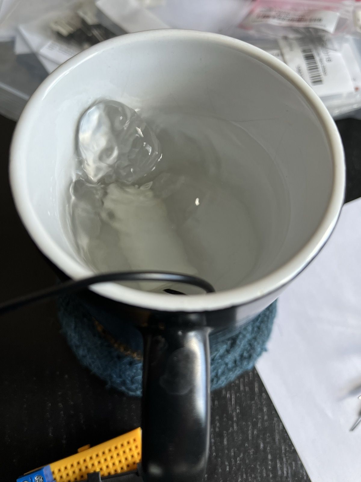 A wire descends into a black mug full of water. At the bottom we can vaguely discern a white cylinder (the pump). The water is bubbling up vigorously at one end of the pump.